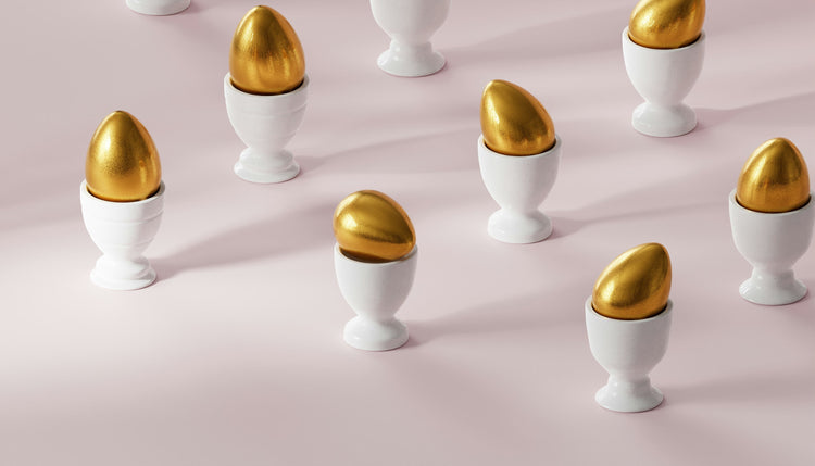Gold eggs in white egg holders across a light pink floor